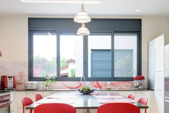 Large charcoal aluminium sliding window in white kitchen with red chairs